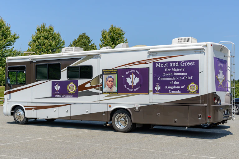 A mobile home with a woman's photo on the side and a sign that reads Meet and Greet Her Majesty Queen Romana Commander-in-Chief of the Kingdom of Canada.