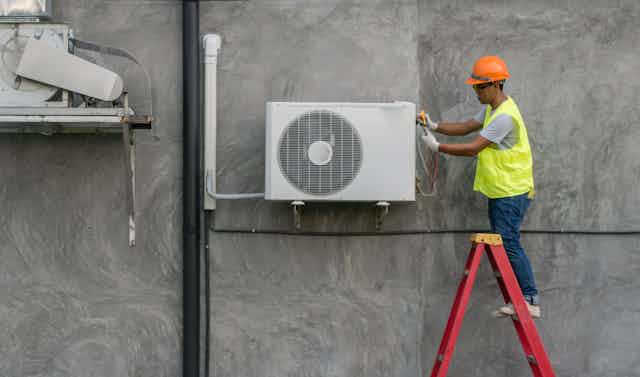 man in high-vis vest fixes air conditioning unit