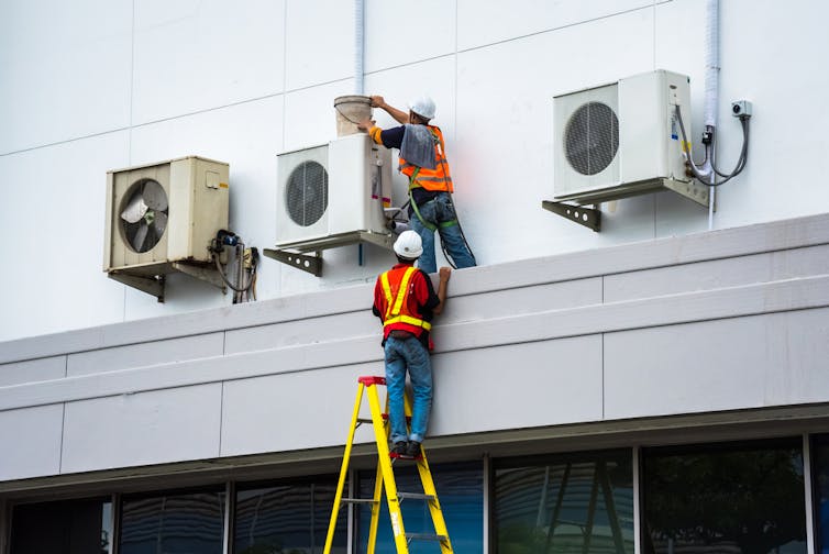 two men servicing air conditioning outside building