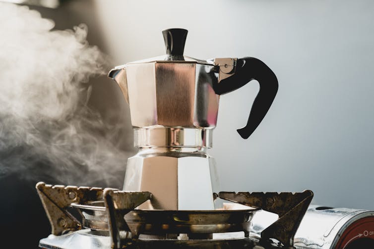 A multifaceted aluminium pot with a black handle, with steam coming from the spout