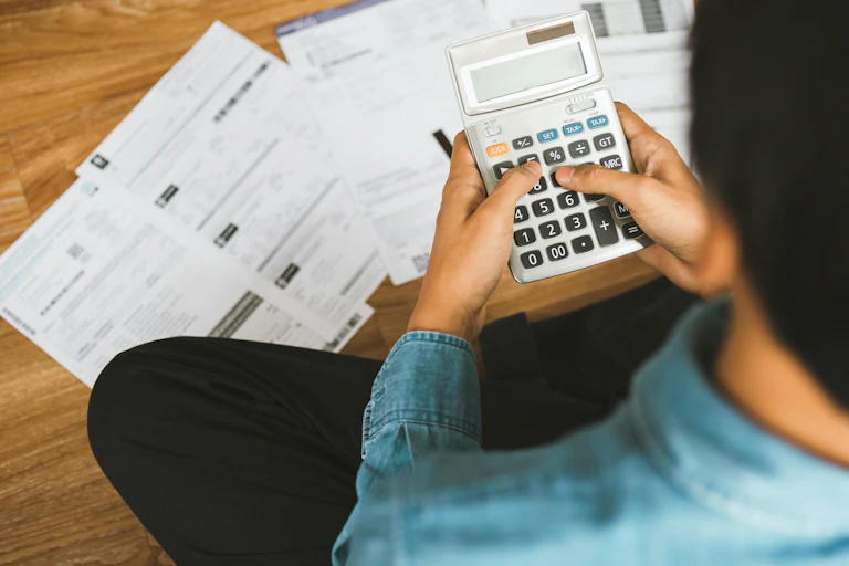 Persona con calculadora y facturas en el suelo.