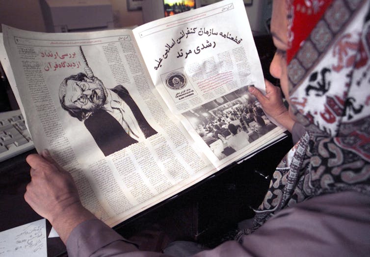 Woman in headscarf holds newspaper.