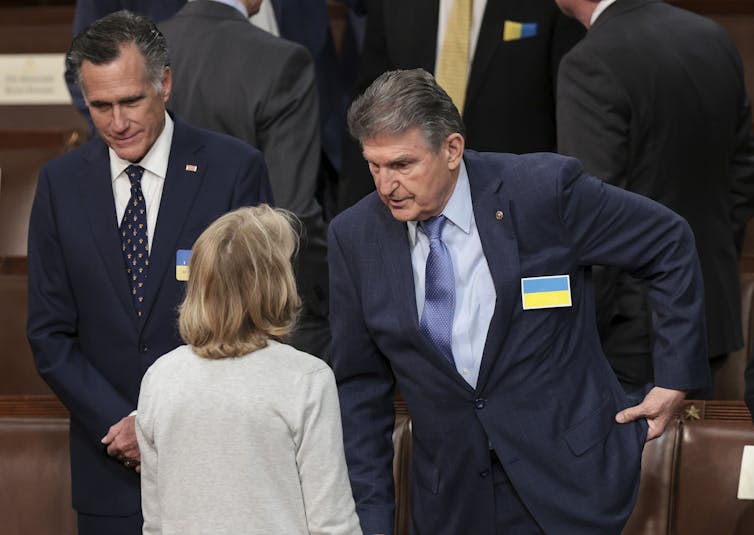 Two men in suits and a woman in a light jacket talking.