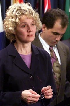 Nancy Olivieri. A woman in a black suit holds a pair of glasses.