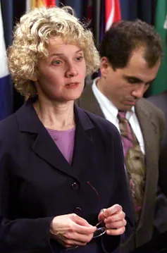 Nancy Olivieri. A woman in a black suit holds a pair of glasses.