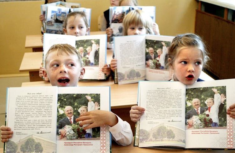 Des enfants dans une classe chantent en montrant une photo d’Alexandre Loukachenko dans leur manuel