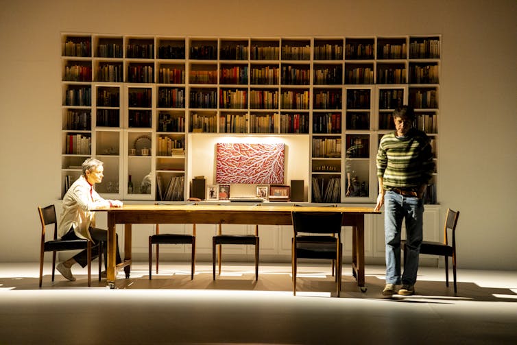 A large dining table and a wall filled with books.