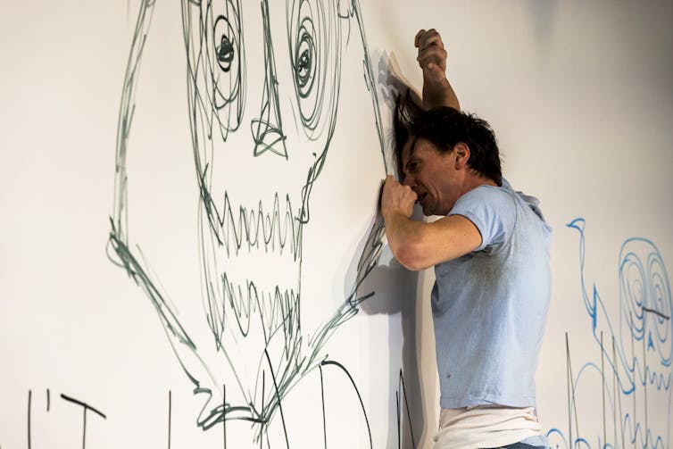 A man leans against drawings on the wall.