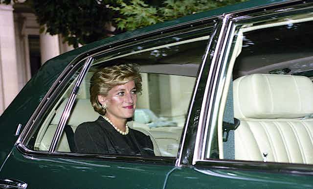 Diana, Princess of Wales smiling and sitting in the backseat of a car, seen through the window