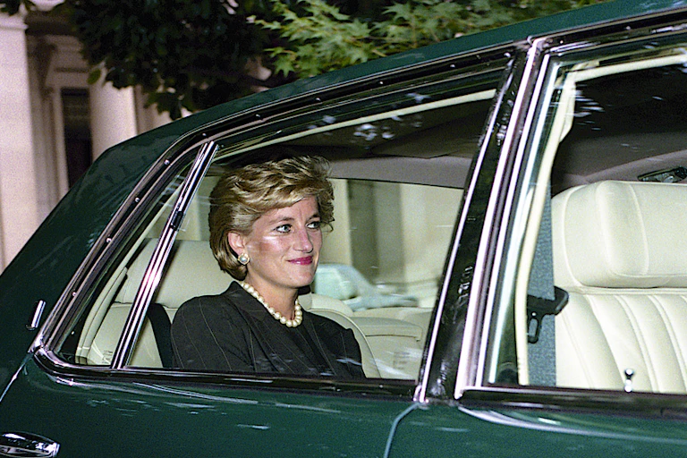 Diana, Princess of Wales smiling and sitting in the backseat of a car, seen through the window