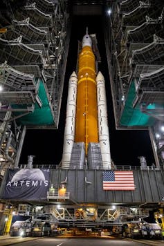 a large rocket with two boosters attached to its sides standing between two massive gantries