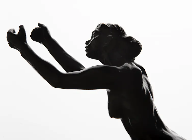 A small bronze statue of woman holding up her arms imploringly.