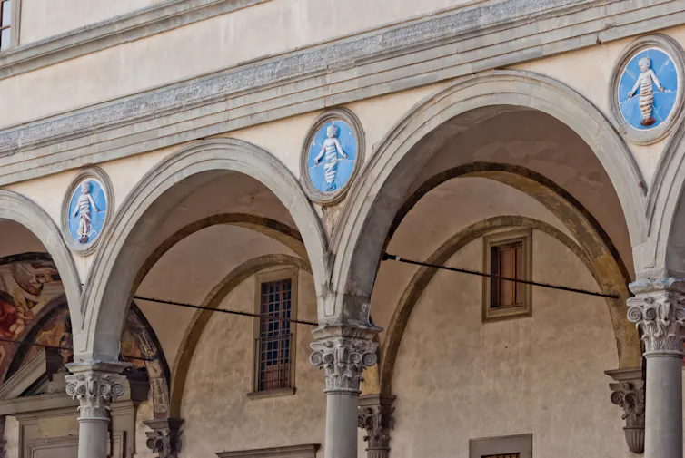Three arches, above the columns are terracotta figures of infants surrounded by a circular blue background.