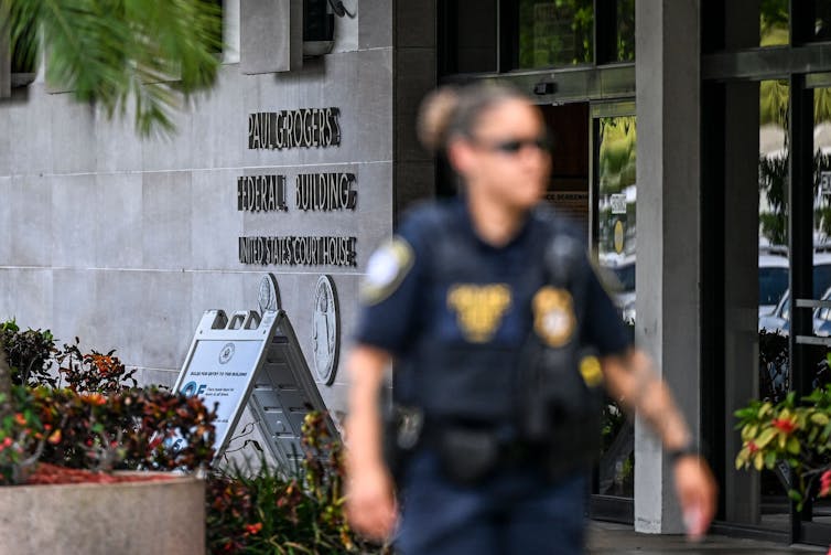 A female security guard or police officer is seen walking outside of a courthouse.