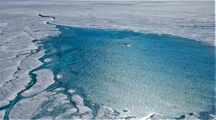 Uma grande área de piscinas de água derretida na superfície nevada da Groenlândia e forma um rio e riachos.