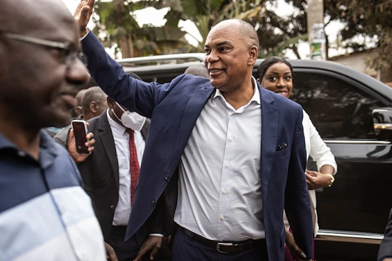 Man wearing grey suit on white shirt, waving at presumed supporters.