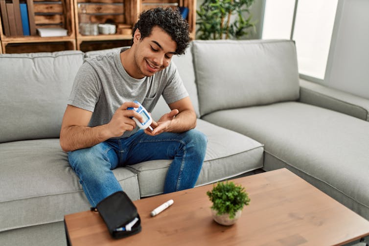 A young man sitting on a sofa testing his blood sugar.