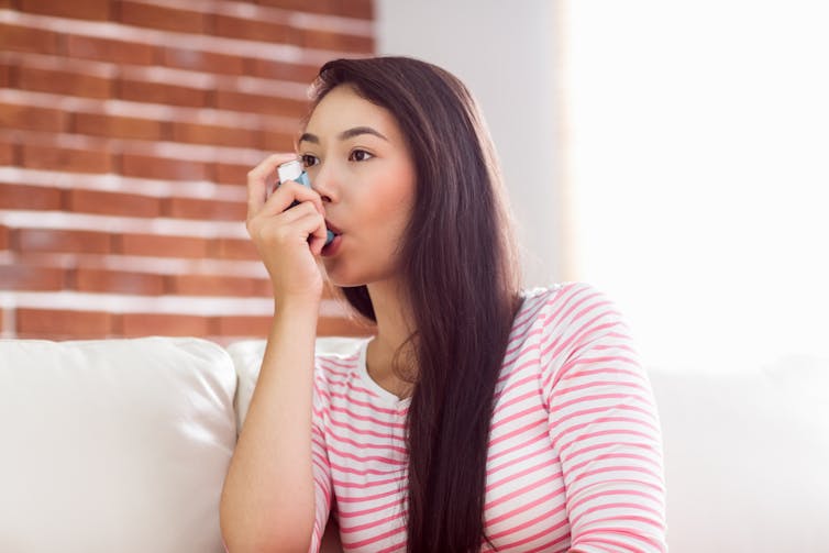A young woman in a pink and white striped shirt using an asthma inhaler