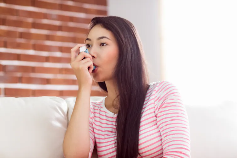 A young woman in a pink and white striped shirt using an asthma inhaler