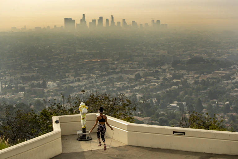 A woman jumps rope at an overlook of Los Angeles, where the city is shrouded in wildfire smoke.