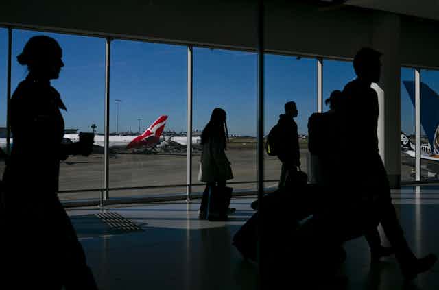 Passengers at an airport with a Qantas plane in the background.