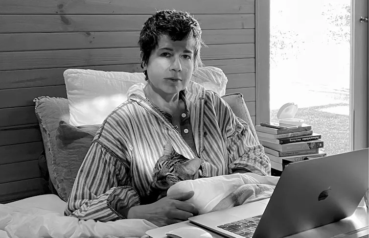 A woman in bed with her cat and a laptop