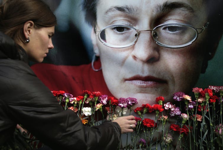 A woman places flowers before a portrait of a woman