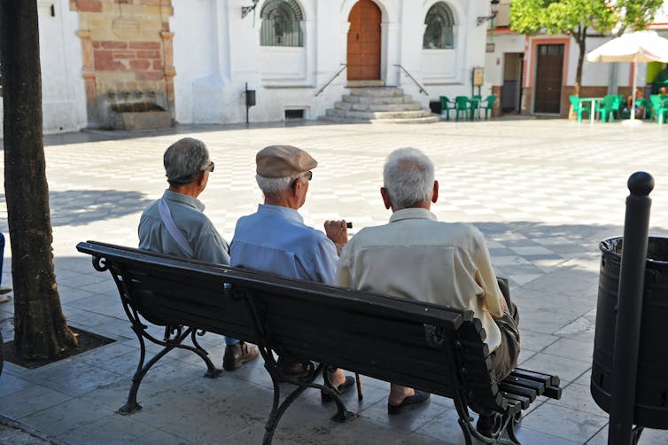 Tres ancianos de espaldas sentados en un banco en un pueblo.