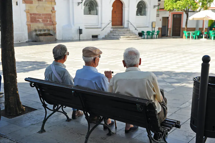 Tres ancianos de espaldas sentados en un banco en un pueblo.