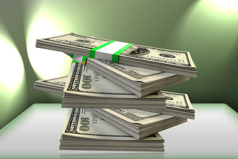 Pile de billets de 100 dollars tenus par des rubans verts.