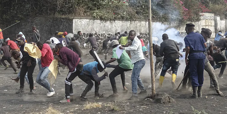 Police and protesters fight in a city street. Smoke is visible.