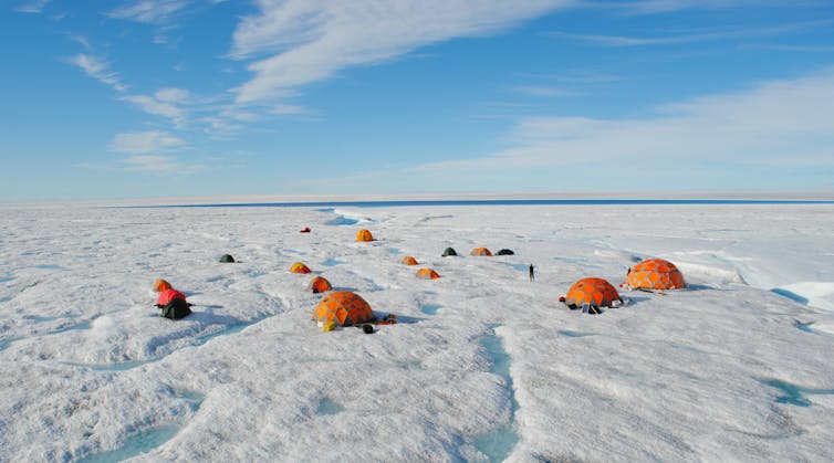 Several brightly colored research tents dot a landscape with streams and snow on the ice cap.