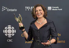 A woman dressed in a black dress holds an award statue.