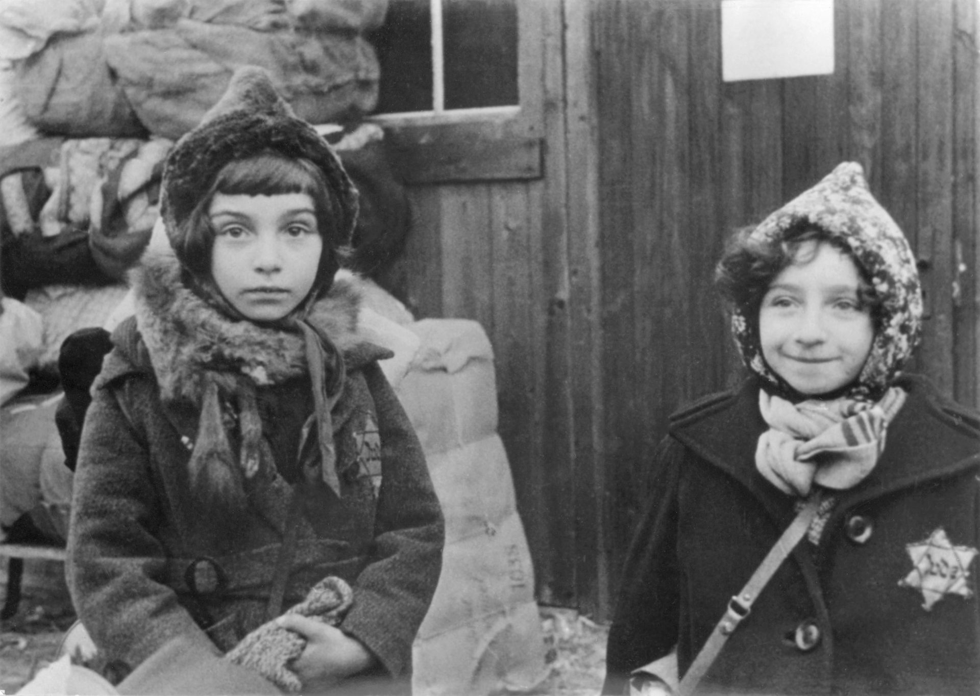 Two young girls in winter coats and hats, both wearing Jewish stars on their coats.