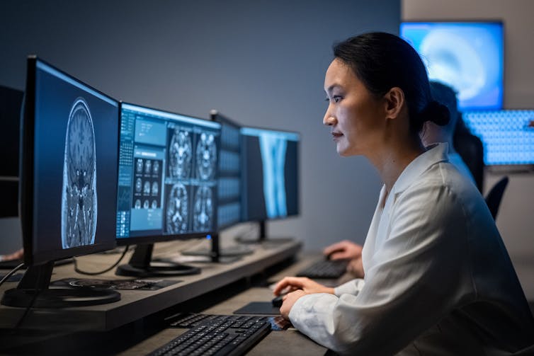 Scientist looking at brain MRIs on multiple computer screens