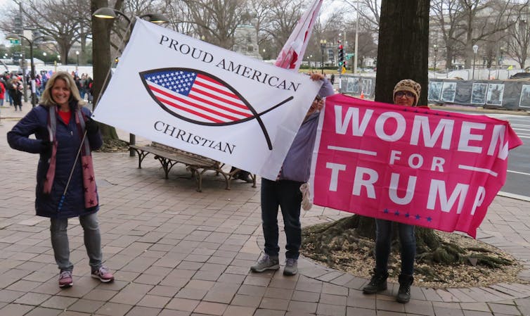 Women stand with banners saying 'Proud American Christian' and 'Women for Trump'