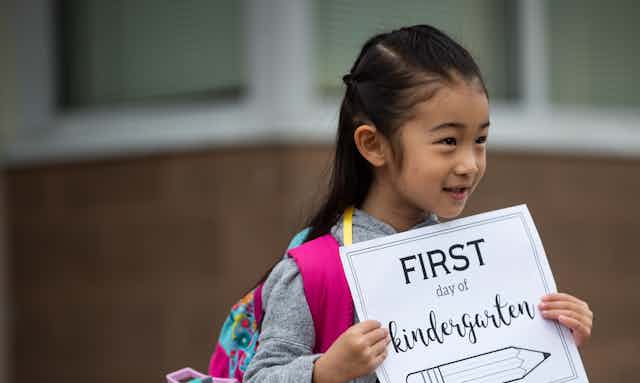 A child is seen holding a sign that says 'first day of kindergarten' 
