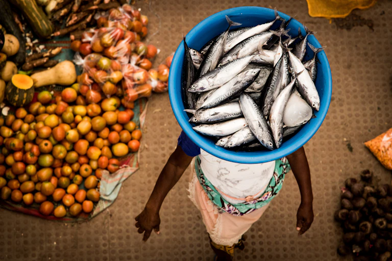 African woman carrying fish in a basket on her head on the local market