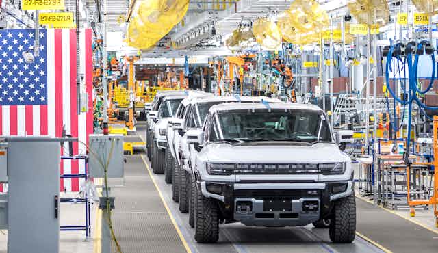 A factory with American flags and bunting with a line of new electric Hummers among the machinery.