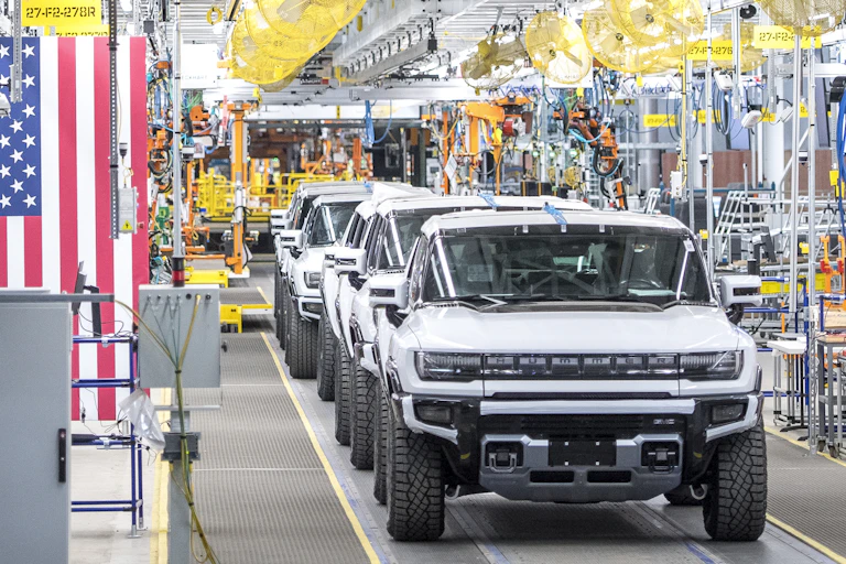A factory with American flags and bunting with a line of new electric Hummers among the machinery.