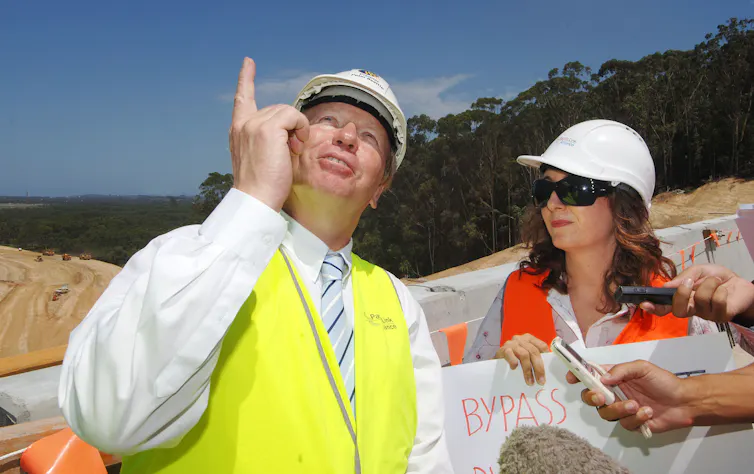Man in hi-viz and hard hat points to sky flanked by woman also in hi-viz and hard hat