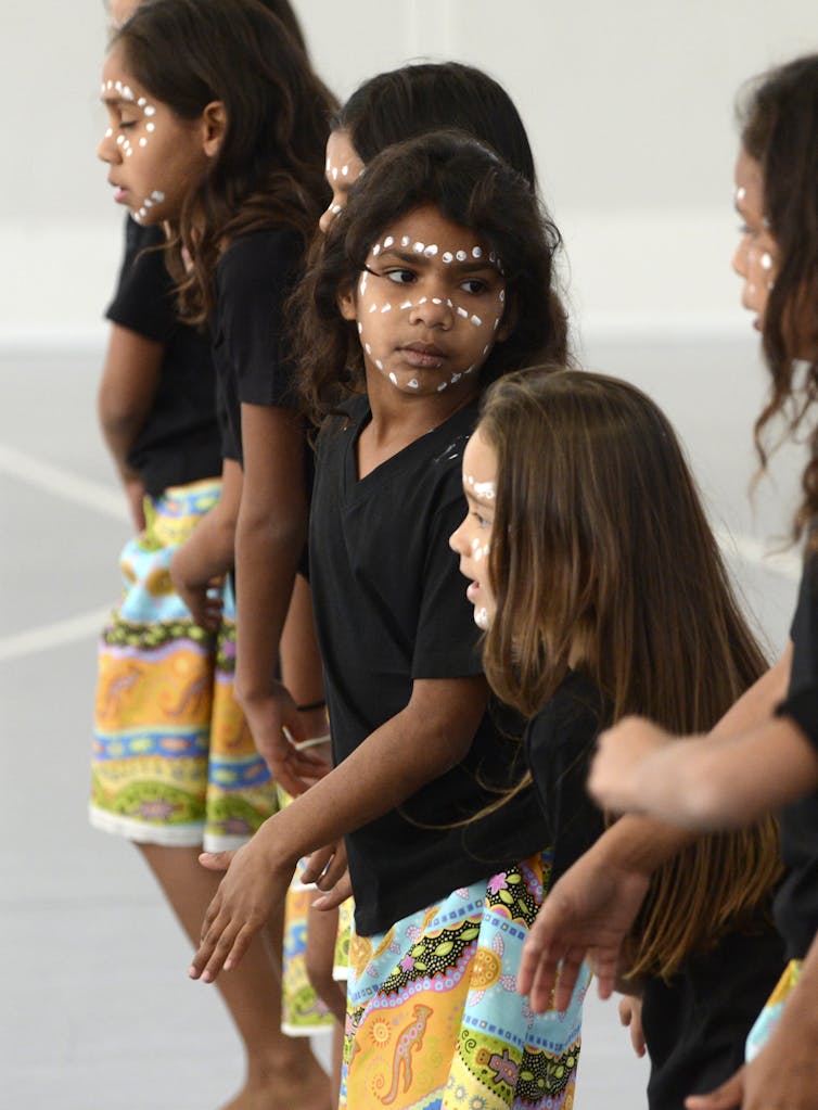 مجموعة من أطفال الأمم الأولى يستعدون للرقص. يرتدون المغرة على وجوههم.