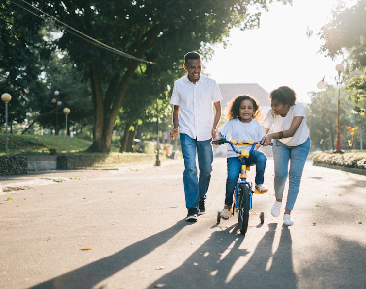 Two adults with a child on a bicycle with training wheels