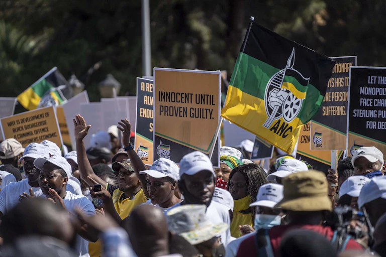 .Men and women in ANC regalia carry placards outside court say 'innocent until proven guilty'