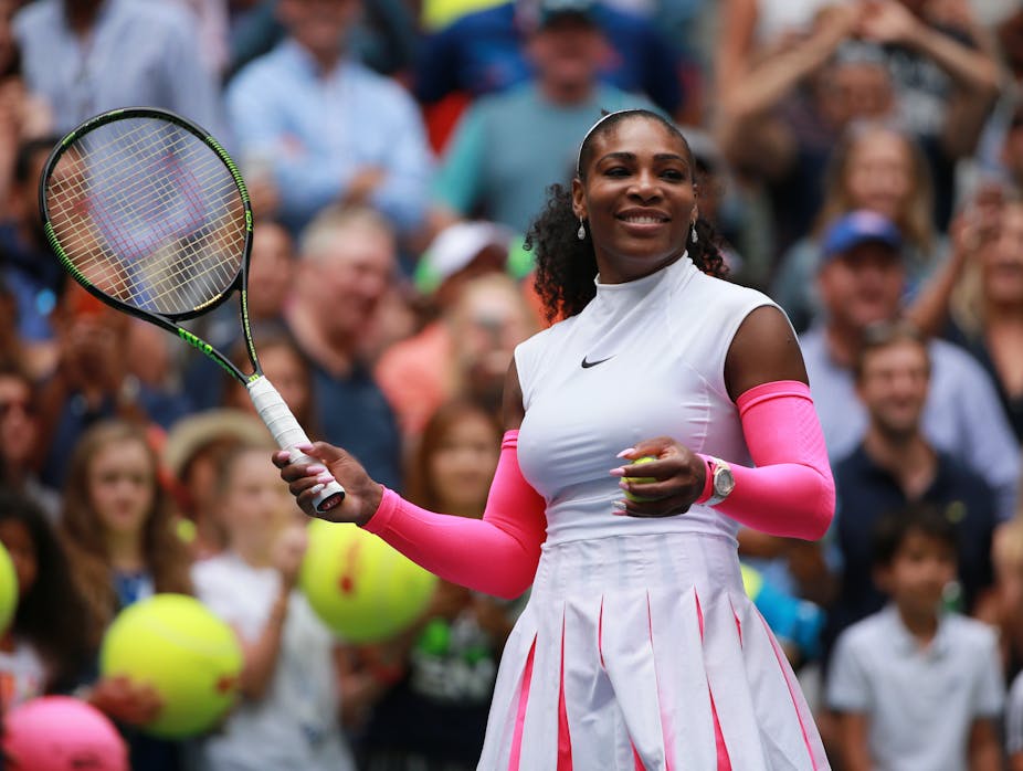 Serena Williams smiles on the court. She is holding a tennis racket in her right hand. 