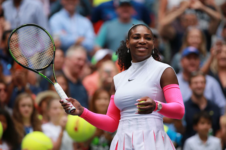 Serena Williams smiles on the court. She is holding a tennis racket in her right hand.