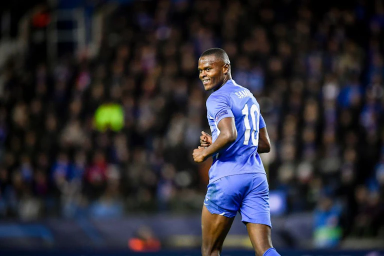 A man in a blue football outfit runs, looking back over his shoulder and smiling.