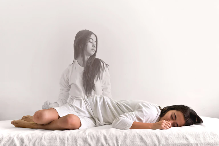 Girl looks down at her body lying on a bed