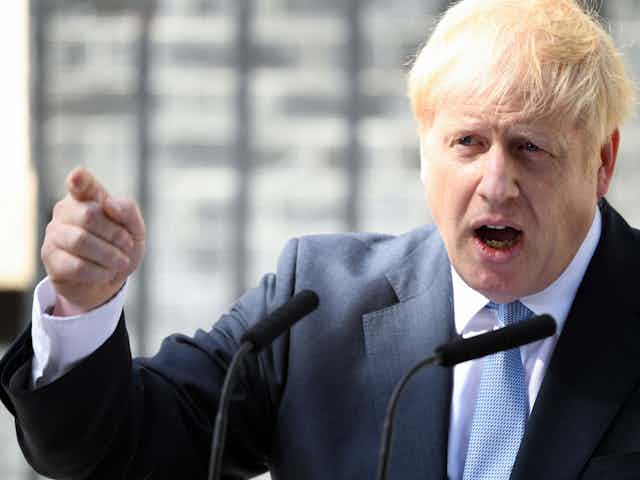 Close up of Boris Johnson gesturing with a pointed finger and speaking into a microphone outside of Downing Street