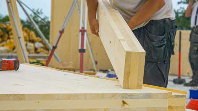 A builder lays an engineered wood beam on to wooden foundations.